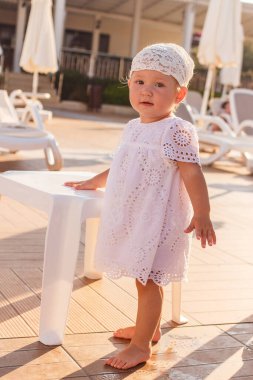 Beyaz eşarplı, bronz tenli tatlı bir kız yazın güneşin altında otel bahçesinde çıplak ayakla duruyor.