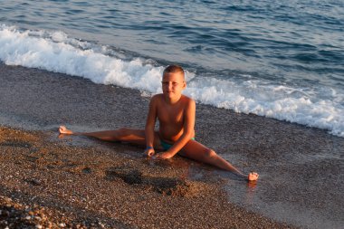 İyi beslenmiş Avrupalı çocuk gün batımında sicimle sahilde oturur..