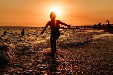 Gün batımında denizde koşan bir çocuğun silueti.