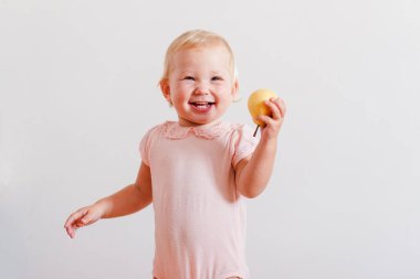 Neşeli sarışın bir yaşındaki kız beyaz arka planda sarı armut yiyor..