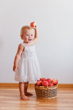 Beyaz elbiseli sevimli bir Avrupalı kız çocuğu ve beyaz arka planda bir sepet kırmızı elma. Hasat ve çocuklar