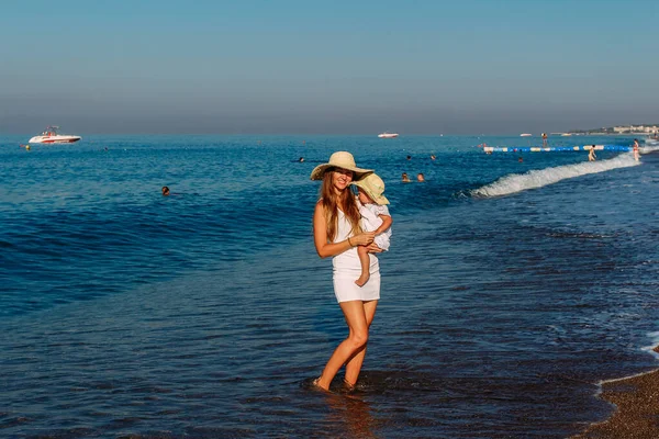 Улыбающаяся Женщина Шляпе Держит Руках Годовалую Девочку Стоящую Летом Море — стоковое фото
