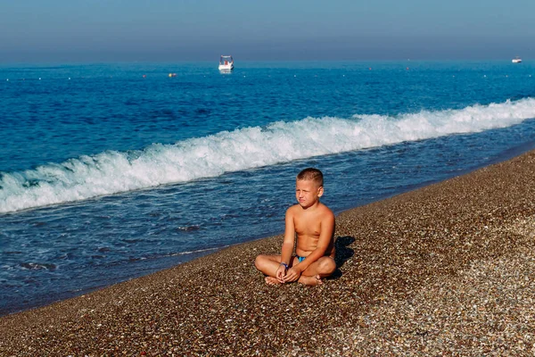 海の小石の海岸には9歳の少年が腰を下ろしている — ストック写真