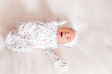 Yeni doğmuş küçük bebek beyaz bir çarşafta yatıyor, yukarıdan bakıyor.