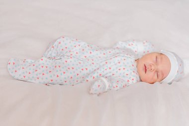 Yeni doğmuş kepli ve tulumlu bir bebeğin beyaz bir çarşafta uyuması çok hoş. Doğumdan bir hafta sonra