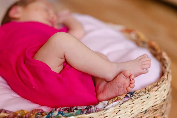 Newborn girl in pink bodysuit barefoot lies in a round crib and sleeps