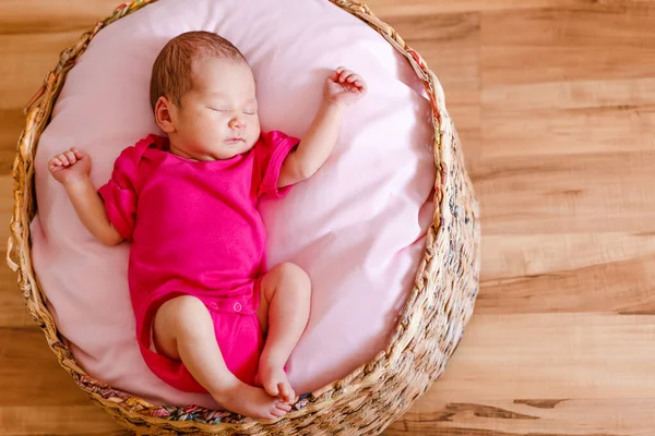 Newborn girl in pink bodysuit barefoot lies in a round crib and sleeps