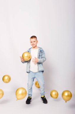 Beyaz arka planda kot pantolon ve altın rengi balonlar giyen 10 yaşında bir çocuk.