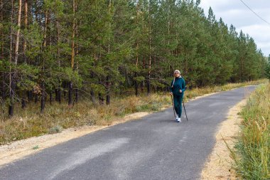 Emeklilik yaşındaki zayıf bir kadın parkta yürüyen İskandinav bir kadınla meşgul..