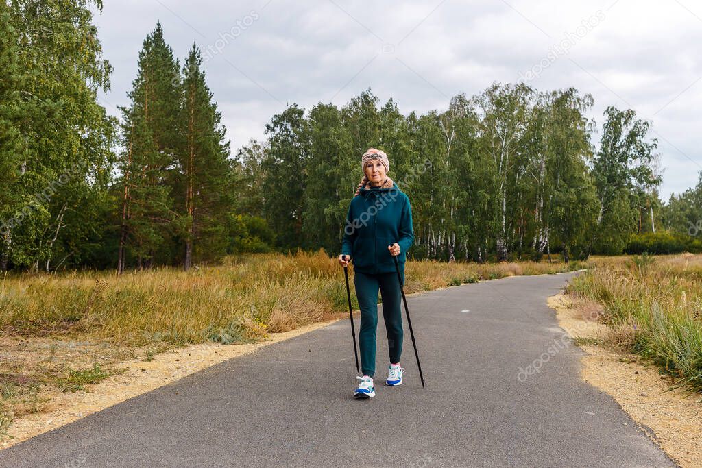 slender woman of retirement age is engaged in Nordic walking in the park.