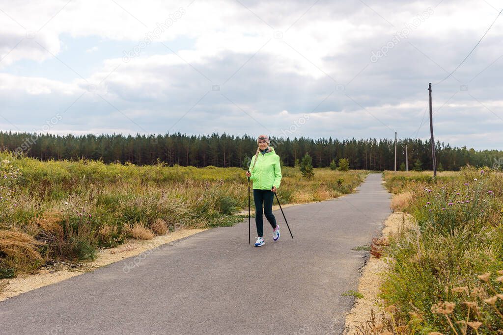 smiling five-year-old woman walks along the track with poles for Nordic walking.