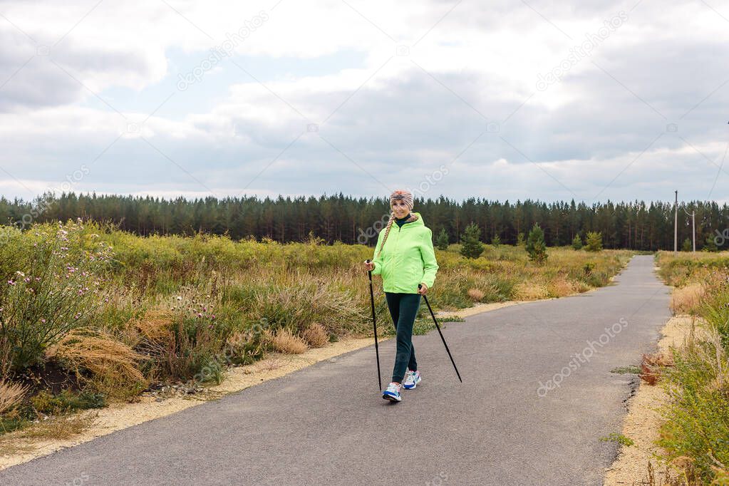 smiling five-year-old woman walks along the track with poles for Nordic walking.