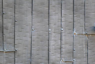 Yüzey, perçinlerle birbirine bağlı siyah çelik plakalardan oluşuyor. Koyu doku veya arkaplan