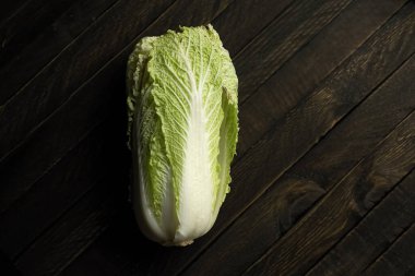 Koyu ahşap bir masanın üzerinde yeşil yapraklı Pekin lahanası var..