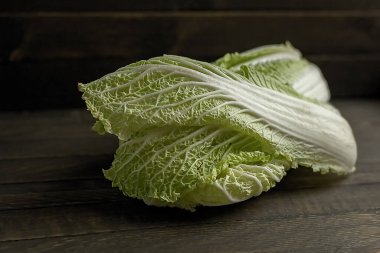 Koyu ahşap bir masanın üzerinde yeşil yapraklı Pekin lahanası var..