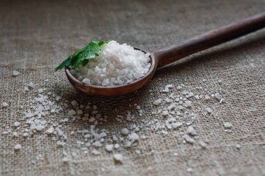 Büyük tuz kristalleri tahta bir kaşıkta yatar. Maydanoz yaprağının yanında..