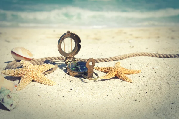 Cross-processed compass with shells and rope on ocean beach — Stock Photo, Image