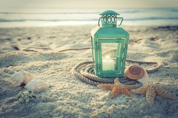 Cross-processed lantern on beach with shells and rope at sunrise — Stock Photo, Image