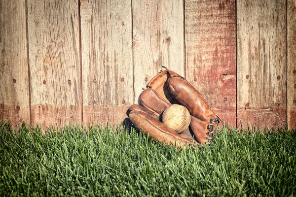 Old baseball mitt and ball on grass against wooden fence — Stock Photo, Image