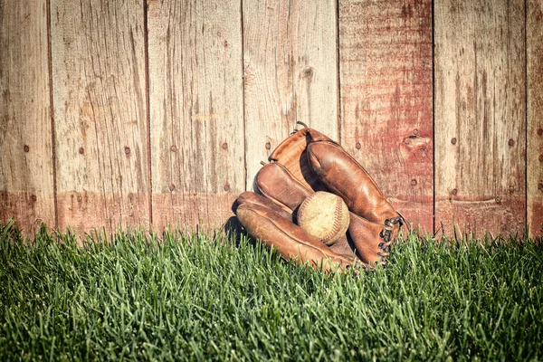 Vieux gant de baseball et balle sur herbe contre clôture en bois — Photo