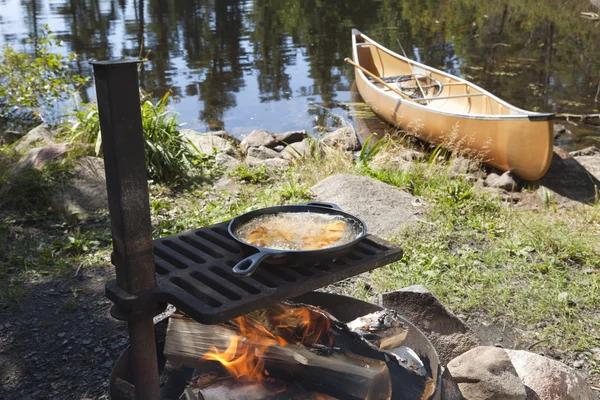 Peixe cozinhando ao ar livre em uma frigideira com uma canoa no backgr — Fotografia de Stock