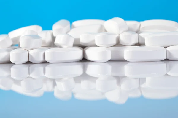 Heap of white pills close up on a blue — Stock Photo, Image