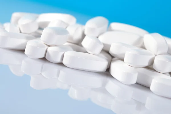 Heap of white pills close up on a blue — Stock Photo, Image