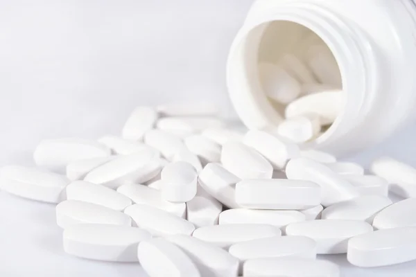 Білі таблетки виливаються з пляшки на білому — стокове фото