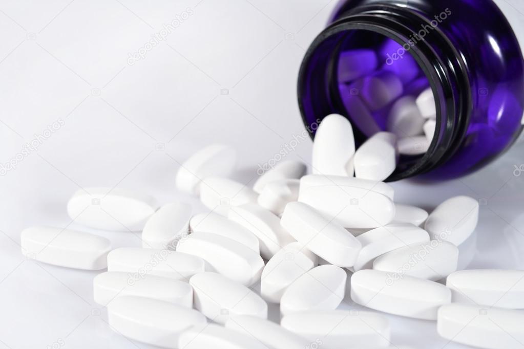 White pills spill out from bottle on a white