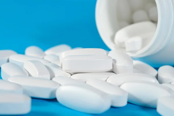 Білі таблетки виливаються з пляшки на синьому — стокове фото