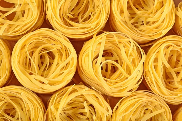 Tagliatelle di pasta italiana cruda nidi come sfondo — Foto Stock