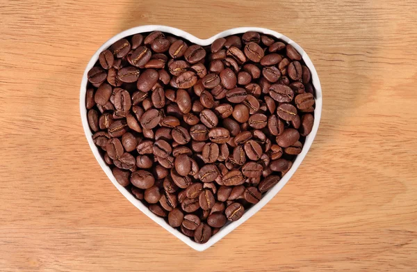 Granos de café en plato en forma de corazón — Foto de Stock