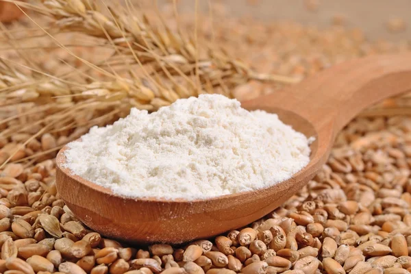 Harina blanca en una cuchara de madera y espigas de trigo en un grano de trigo —  Fotos de Stock
