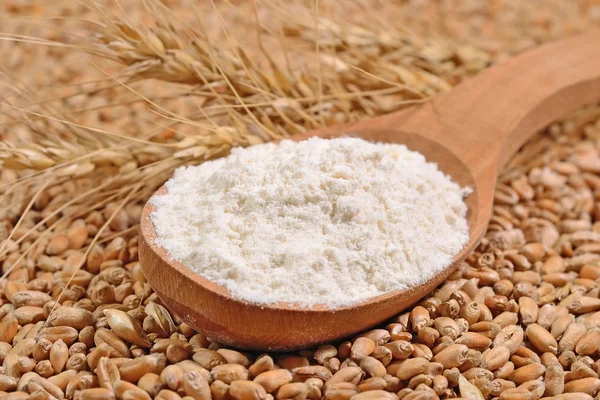 Farinha branca em uma colher de madeira e orelhas de trigo em um grão de trigo — Fotografia de Stock
