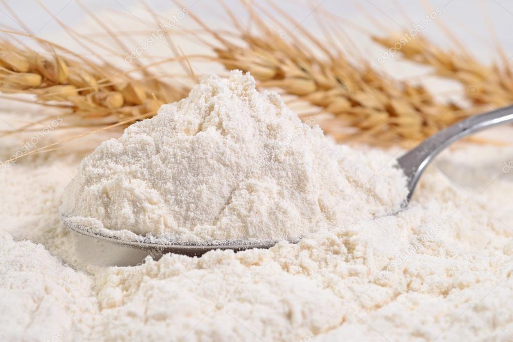 White flour in a spoon and ears of wheat 