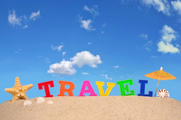 Travel letters on a beach sand against the blue sky