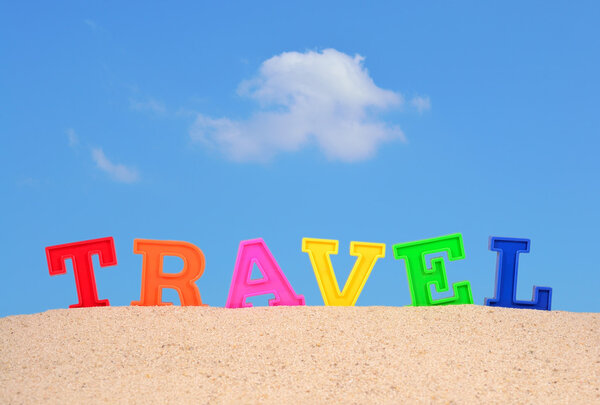 Travel letters on a beach sand against the blue sky
