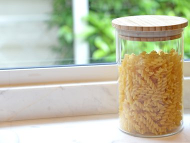 Mutfak penceresi ile ahşap masa üzerinde cam şişelerde pişmemiş makarna çeşitleri