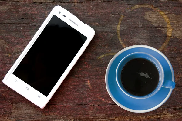 Handy und Kaffeetasse auf Holztisch im Büro — Stockfoto