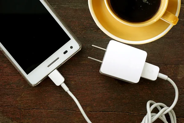 Kaffee, Mobiltelefon und Netzkabel auf Holzboden — Stockfoto