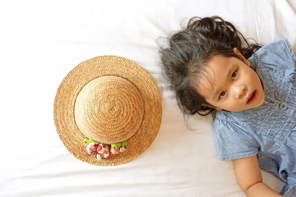 Kleine asiatische Mädchen liegend auf Bett mit Hut — Stockfoto