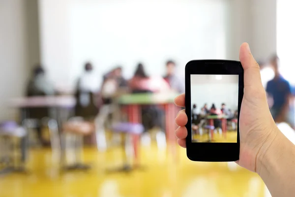 Mão segurar smartphone com sala de aula azul como fundo — Fotografia de Stock