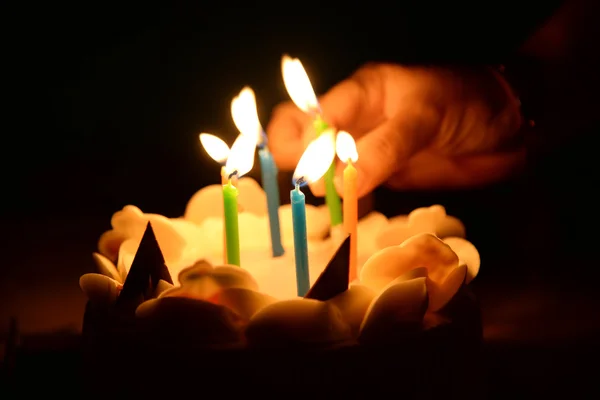 Anniversary cake with hand burning candles in dark — Stock Photo, Image