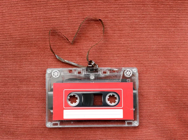 Vintage audio cassette with loose tape shaping a heart on red background — Stock Photo, Image