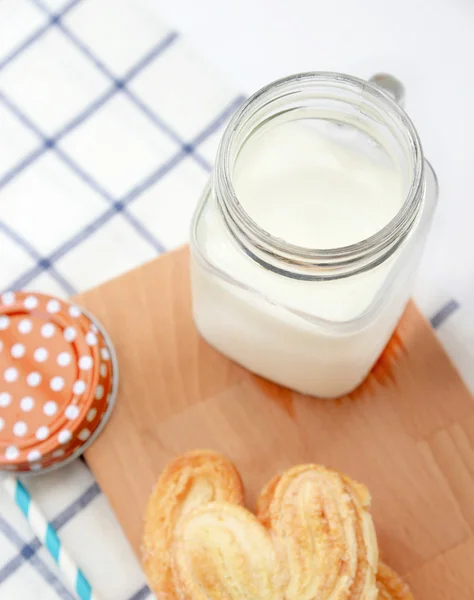 Jug of milk on wooden plate with biscuit — Stock Photo, Image