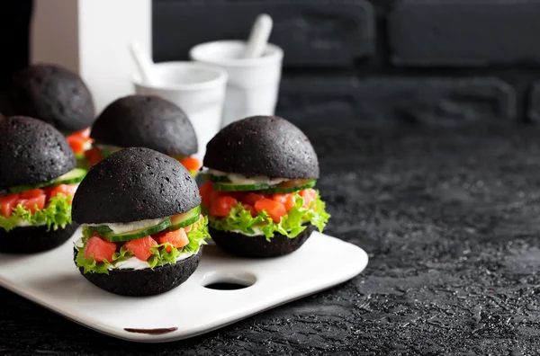 Black burger with smoked salmon tartare, cucumber, lettuce and cream cheese — Stock Photo, Image