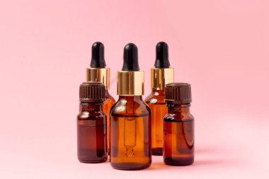 Gerekli yağlar ve kozmetik ürünleri için kehribar bir şişe taşın yanında duruyor. Pembe arka planda cam şişe. Damla, sprey şişesi. Doğal kozmetik konsepti.