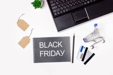 Kara Cuma. Dizüstü bilgisayar, not defteri ve beyaz arka planda alışveriş arabası. Çevrimiçi alışveriş kavramı