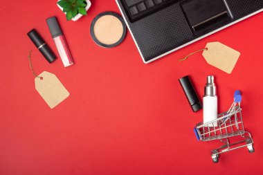 Laptop, alışveriş arabası ve kozmetik ürünleri parlak kırmızı arka planda. Çevrimiçi alışveriş kavramı