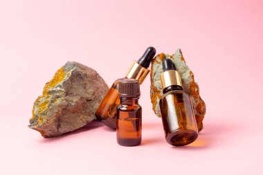 Gerekli yağlar ve kozmetik ürünleri için kehribar bir şişe taşın yanında duruyor. Pembe arka planda cam şişe. Damla, sprey şişesi. Doğal kozmetik konsepti.